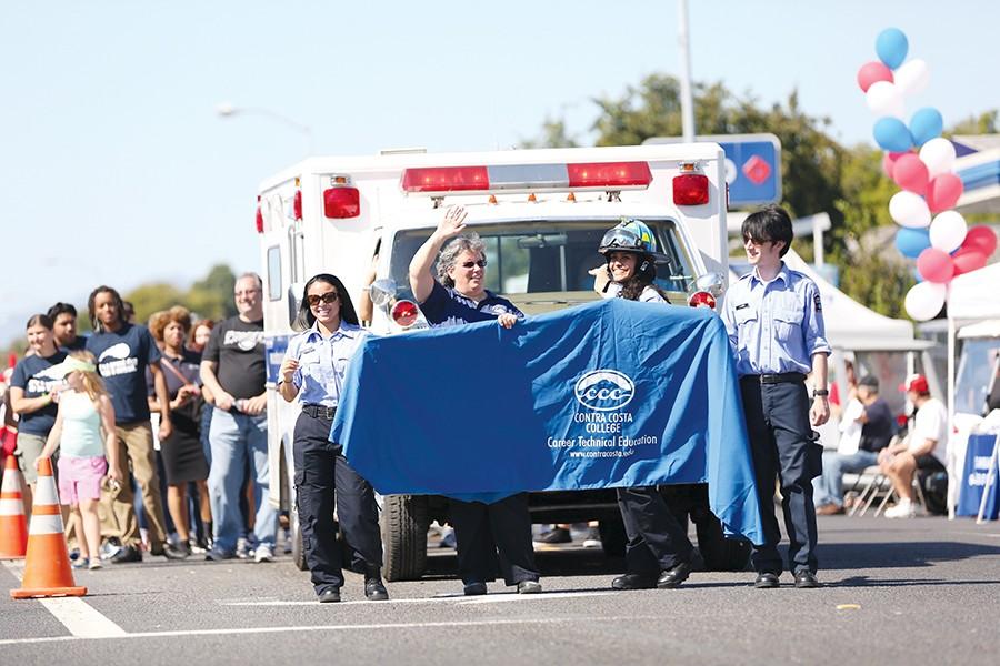 Contra Costa College volunteers wave to spectators during the parade at the El Sobrante Stroll on San Pablo Dam Road on Sunday. CCC showcased its ambulance followed by a trail of students and faculty.