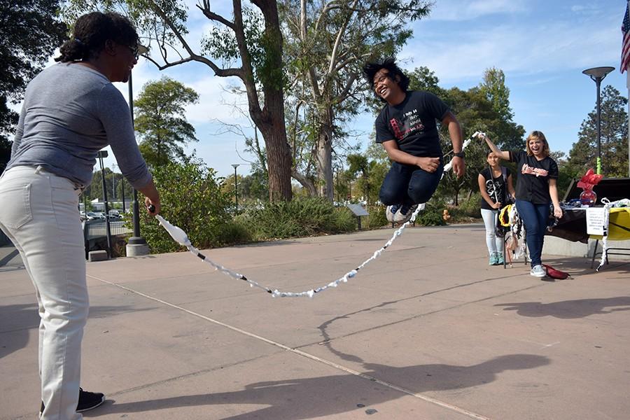 Brandman University representative Jamel Thompson (left) spins the rope as computer science major Francis Sanson (center) jumps through it as sociology major Deija Rothenberg (far right) holds the other handle during the Jump for Jamaica event at the Student Services Plaza on Thursday.