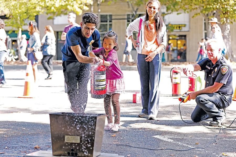Berkeley High School student volunteer Nehar Ali chaperons Wendy Xia’s daughter as she quells a simulated trash can fire during the Sunday Streets event on Shattuck Avenue in Berkeley Sunday. The demonstration was provided by the Berkeley Fire Department.