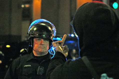 An Oakland police officer watches as a protester points his middle fingers at him during a protest against the Donald Trump presidency in downtown Oakland, Calif. on Thursday, Nov. 10, 2016.
