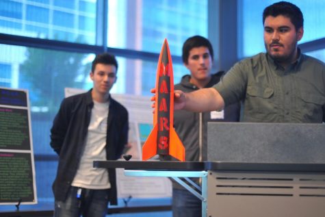 Engineering major Manuel Ayala (right) presents a rocket his team worked on during the semester during the inaugural Student Research Symposium event held in Fireside Hall on May 4.