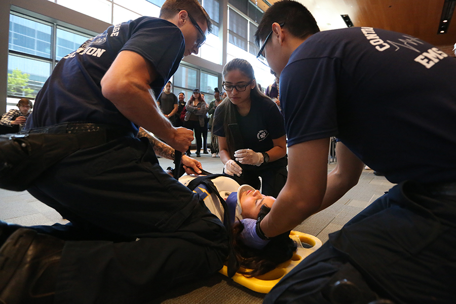 Pre-med student Alex Aquino (right), nursing major William Tucker (left) and fire science major Grechen Medel (center) perform a spinal immobilization demonstration for the crowd on administration of justice major Karla Polanco during a press conference in the Fireside Hall on Monday.