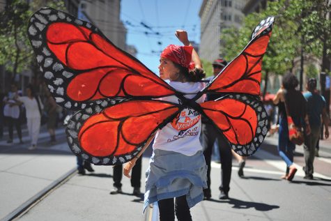 San Francisco residents Velinda Wallace raises her fist during May Day march from Justin Herman Plaza to the Civic Center in San Francisco on Monday. Wallace symbolizes the beauty of migration by the butterfly wings she wears. 