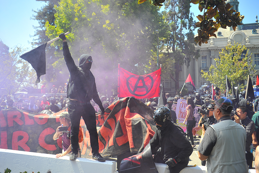 A masked anti-fascist protester holds up a flag as hundreds of anti-facist protesters march unto Martin Luther King Jr. Civic Center Park with a sign reading Smash Racism to counter protest the No to Marxism in America rally on August 27 in Berkeley, California.