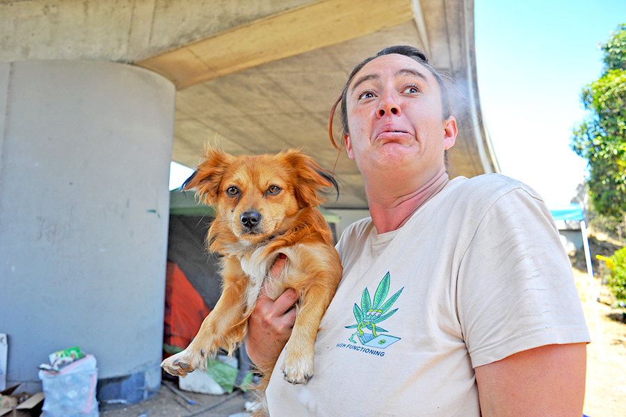 Berkeley resident Rebecca Fisher exhales after smoking a cannabis pre-rolled joint fom the Munchie Movement while holding her dog under the University Avenue exit in Berkeley on Friday. 
