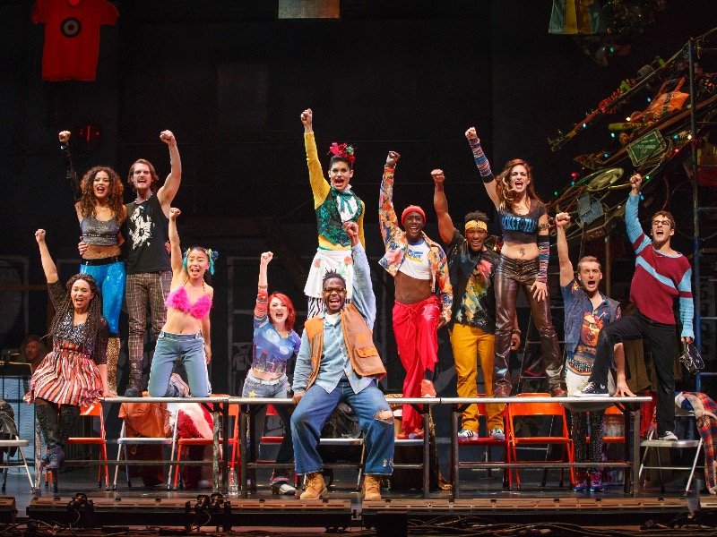 Cast members of Fox’s “Rent” live raise their fists in solidarity for those dying from AIDS during the musical number “La Vie Boheme.”