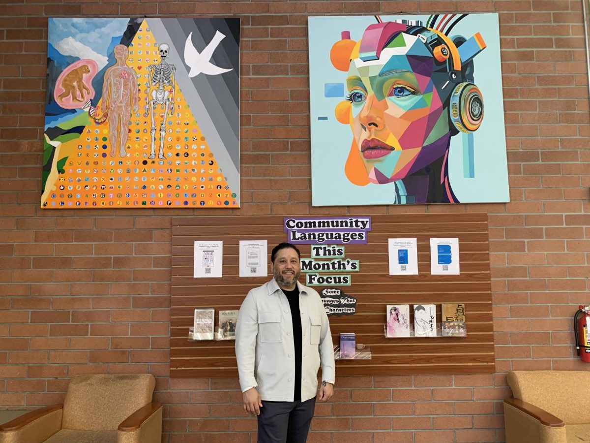 Artist Luis Mercado stands next to two of his paintings, "Back Then till' Now" (left) and "Future-Gen" (right) in the library at Contra Costa College in San Pablo, CA, Thursday, March 6, 2025.