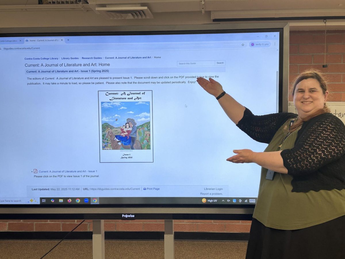 Amy Catania standing in front of a pro-wise board showing off the fist edition of “The Current: A Journal of Literature and Art,” in the library on March 12, 2026 at 2:37p.m. 