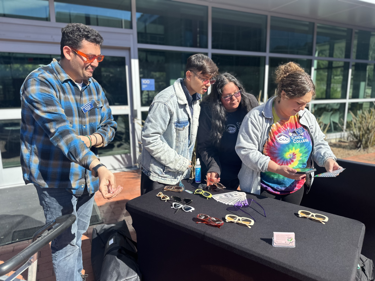 Gabriel Franco, Sanskar Rana, Pamela Fuentes, and Program Coordinator Angela Loera stand at the photo-booth table at Contra Costa College's Spring Club Rush. The group looks at a page of stickers which were used for students' Club Rush Passports. Students visited clubs' tables and received stickers following an incentive of free food upon a completed passport. San Pablo, Calif., Feb. 27. 